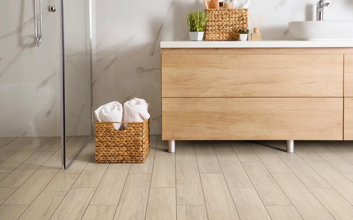 Light tile flooring in a modern bathroom with a wood vanity and glass shower | Kay Riley Carpet & Flooring