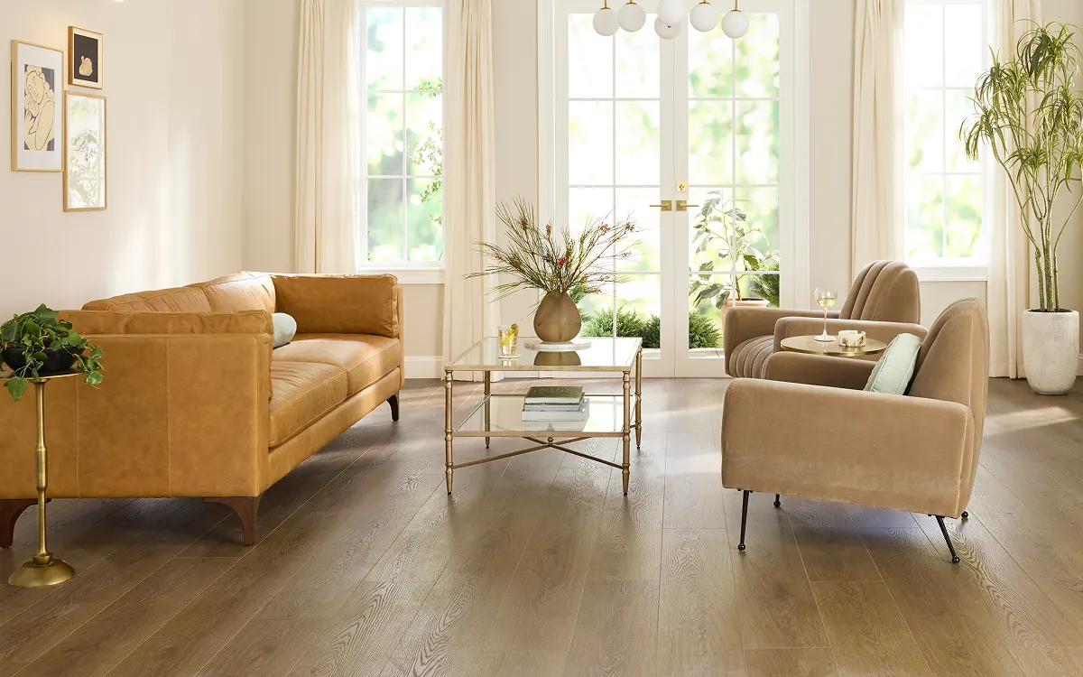 Warm wood flooring in a bright living room with a sofa, armchairs, and large windows | Kay Riley Carpet & Flooring